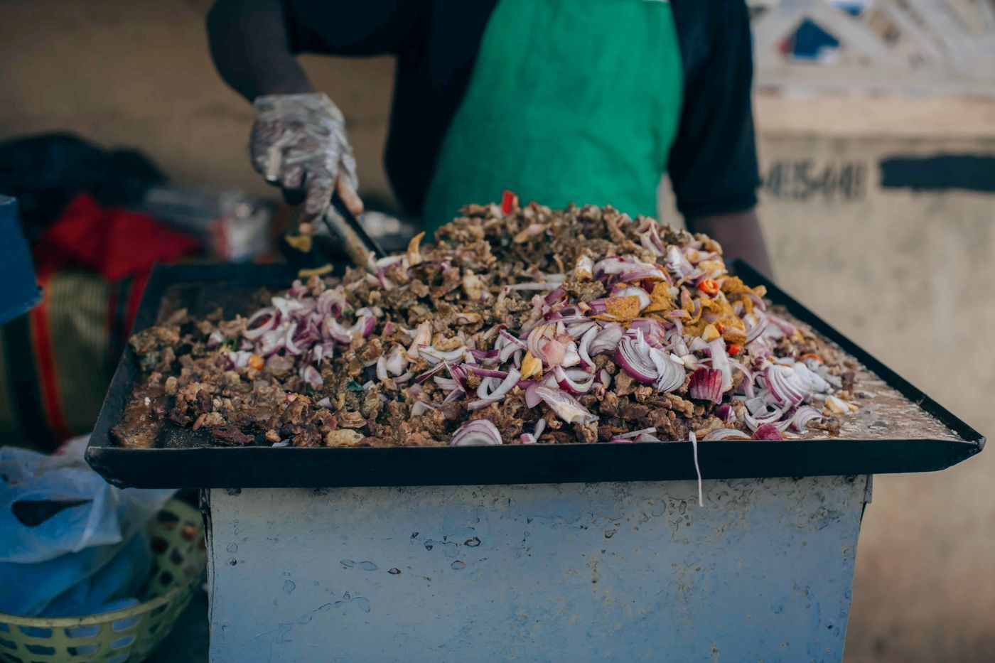 A street-food cook preparing browned meat and red onion on a large griddle
